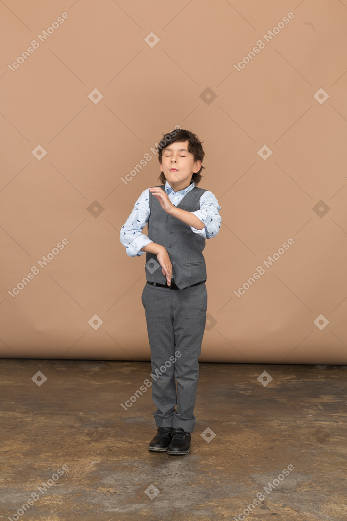 Front view of a cute boy in suit standing with closed eyes and gesturing