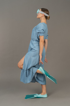 Side view of young woman standing on one leg in snorkelling mask and flippers