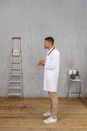 Side view of a gesticulating young doctor standing in a room with ladder and chair