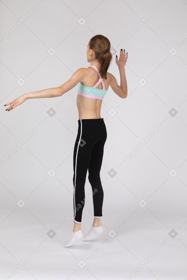 Vue arrière des trois quarts d'une adolescente en tenue de sport en levant la main et en sautant