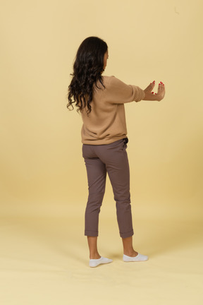 Three-quarter back view of a dark-skinned young female outstretching hands