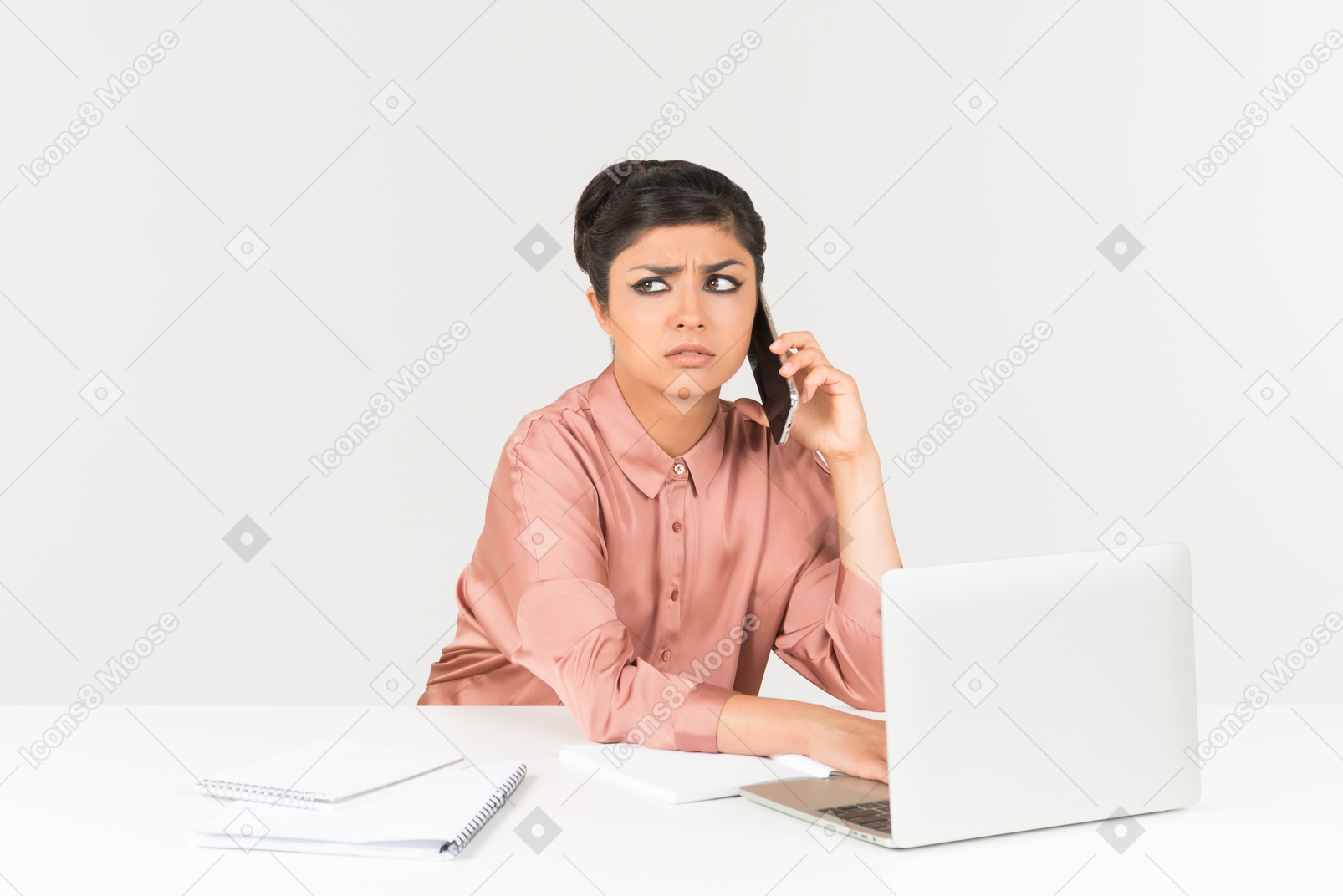 Bothered looking young indian woman talking on the phone and working on laptop