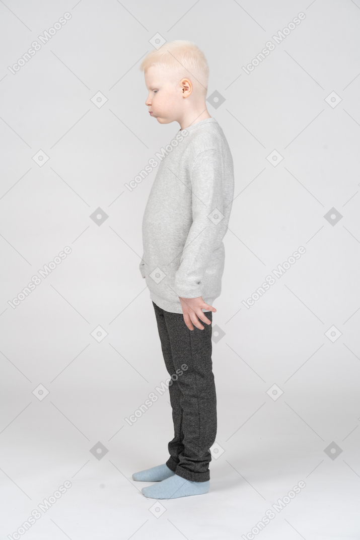 Side view of a blonde kid boy in casual clothes blowing cheeks while looking down