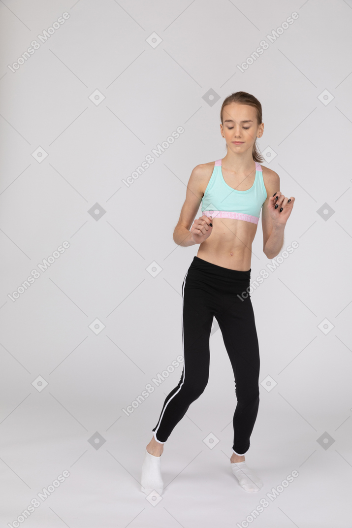 Front view of a teen girl in sportswear dancing and raising her arm