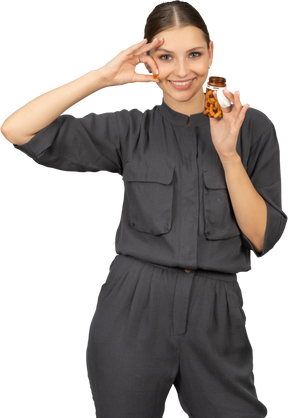 Vue de face d'une jeune femme en combinaison prenant des pilules dans un bocal