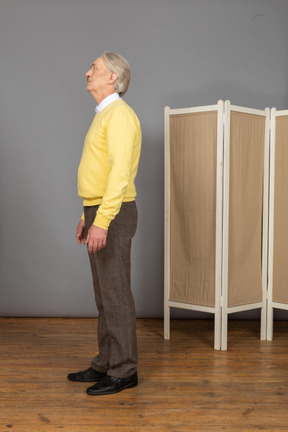 Side view of a nervous old man standing while pressing lips