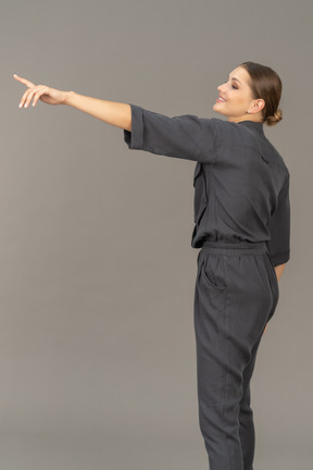 Side view of a cheerful young woman in a jumpsuit outstretching her arm