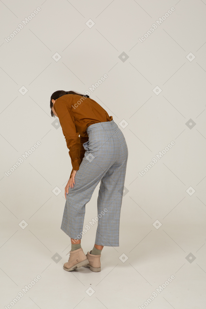 Vista posterior de tres cuartos de una joven mujer asiática en calzones y blusa inclinada hacia adelante