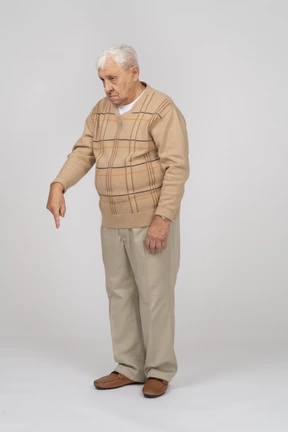 Front view of an old man in casual clothes pointing down with finger