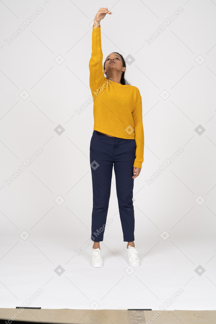 Front view of a girl in casual clothes standing with raised arm and looking up