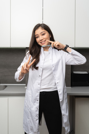 Front view of a smiling female dentist showing a peace sign and holding a toothbrush while looking at camera