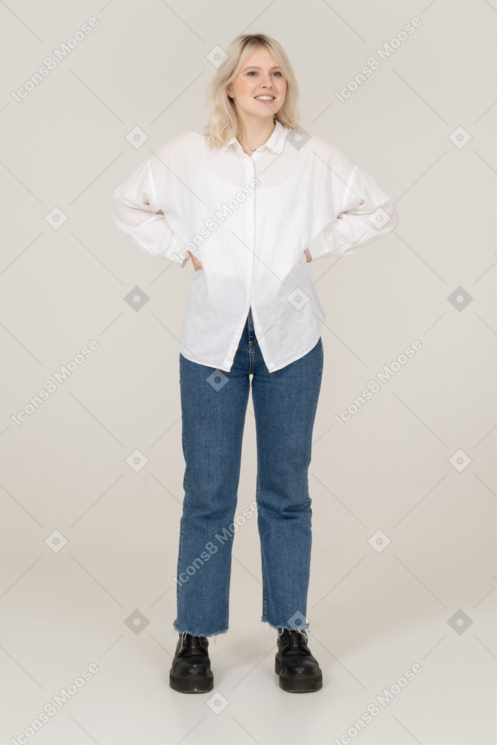 Front view of a blonde female in casual clothes putting hands on hips and looking aside