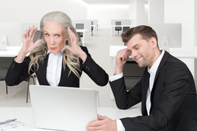 A smiling man sitting at a computer next to a distressed woman