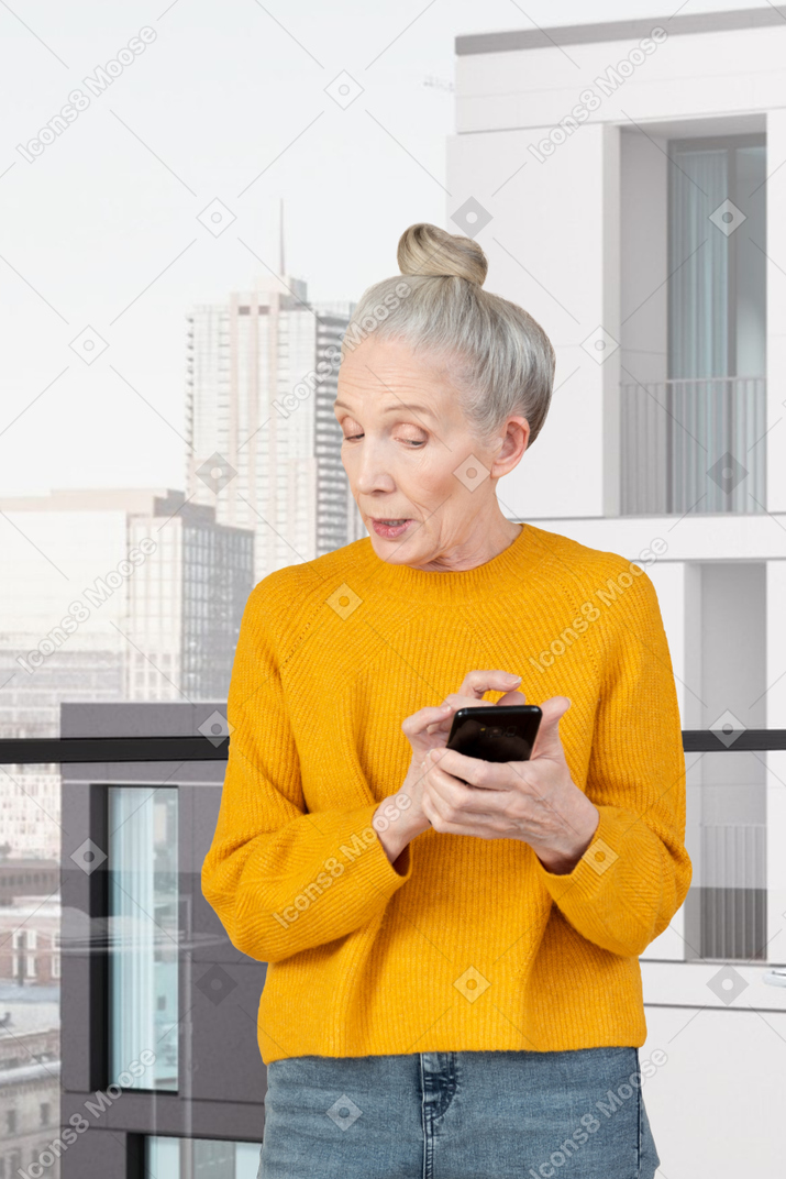 A woman in a yellow sweater looking at a cell phone