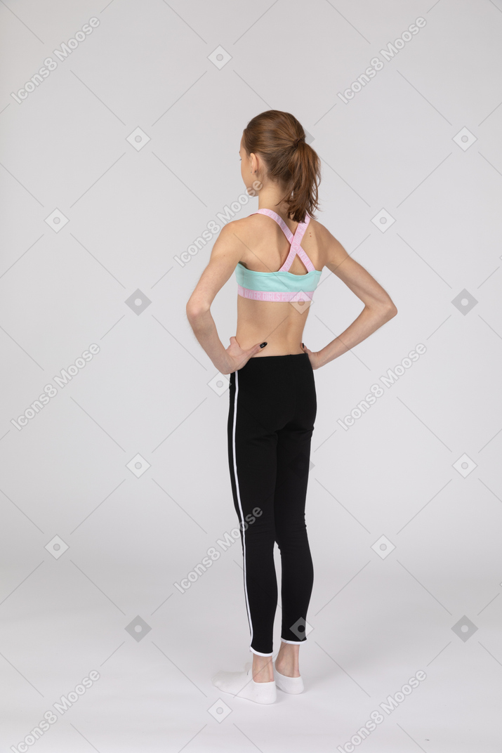 Three-quarter back view of a teen girl in sportswear putting hands on hips