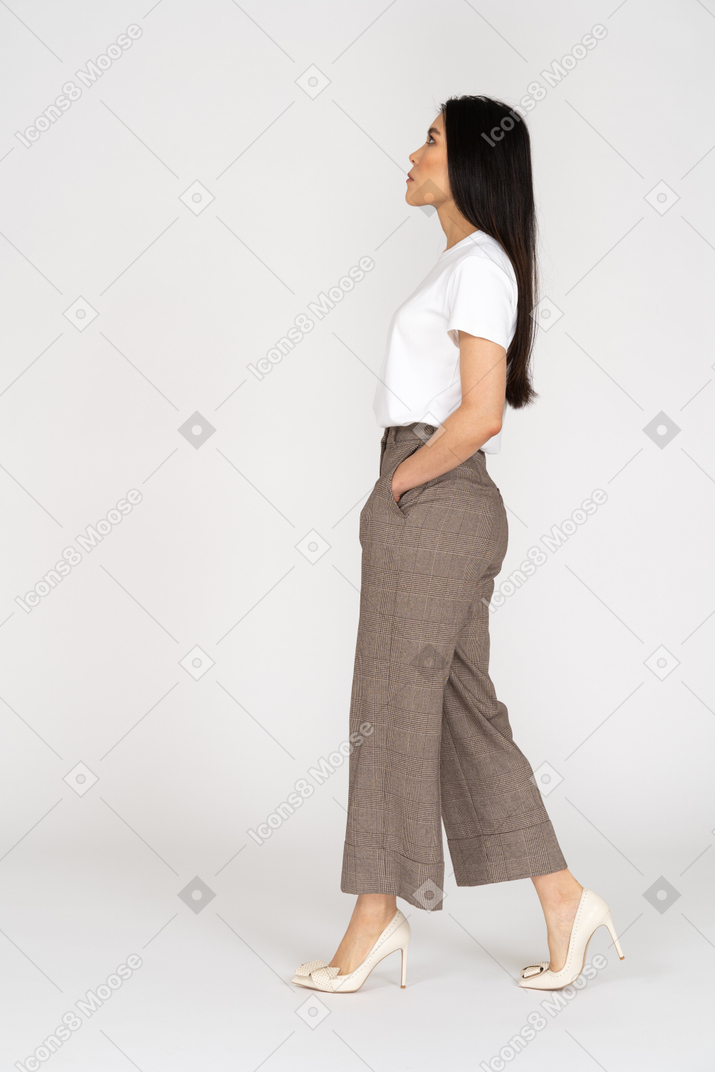 Vista laterale di una giovane donna che cammina in calzoni e t-shirt alzando lo sguardo
