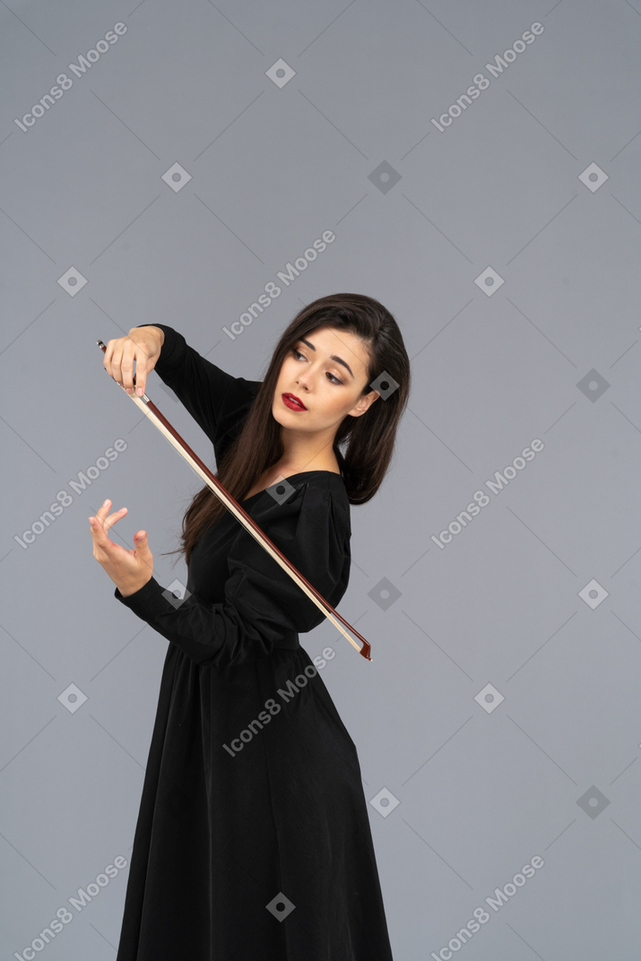 Dreiviertelansicht einer jungen dame in schwarzem kleid, die den eindruck erweckt, geige zu spielen