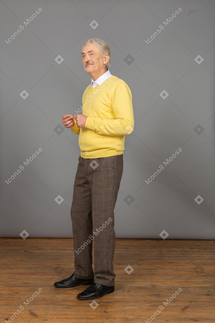 四分之三的观点，一个老男人微笑着穿着黄色套头衫，将手放在一起