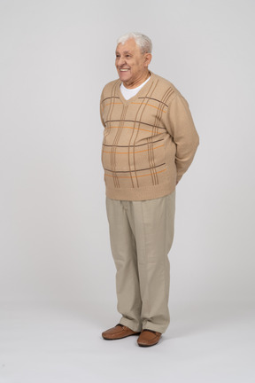 Front view of a happy old man in casual clothes standing with hands behing back