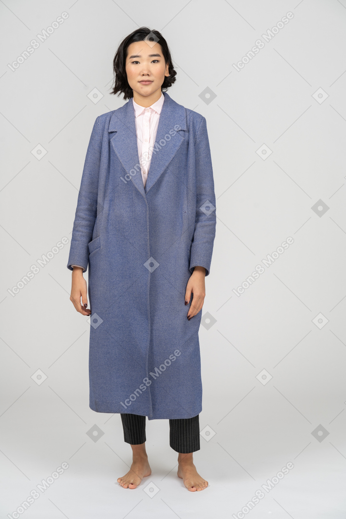 Frau in einem blauen mantel, die mit den armen an den seiten steht