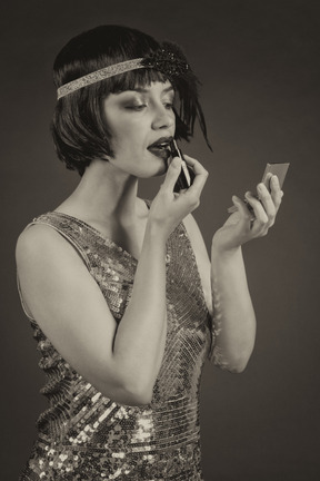 Well-dressed vintage style female applying a lipstick while looking at hand mirror