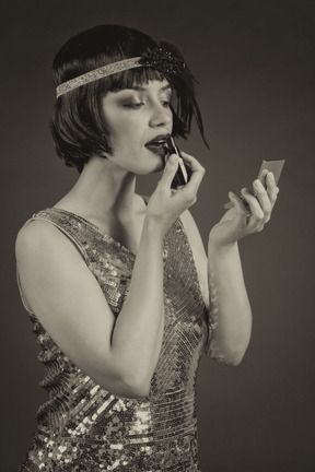 Mujer de estilo vintage bien vestida aplicando un lápiz labial mientras mira el espejo de mano