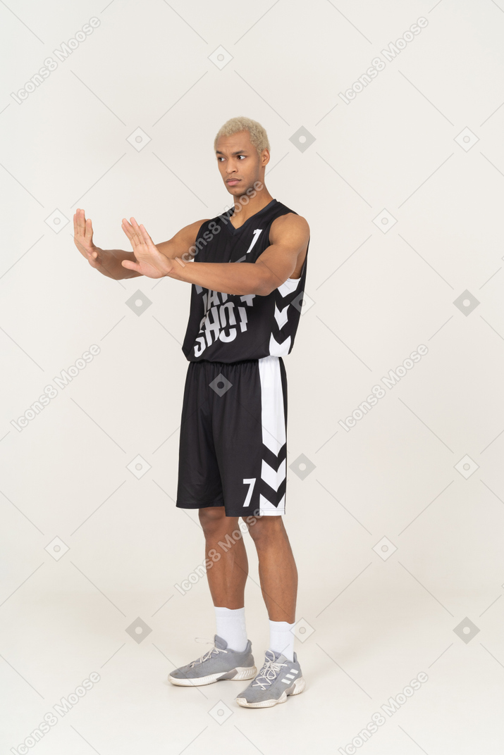 Vista de três quartos de um jovem jogador de basquete do sexo masculino recusando, estendendo os braços
