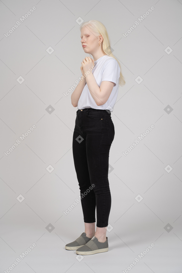 Vista di tre quarti di una giovane donna in abiti casual in piedi con le mani giunte