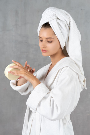 Retrato de una mujer en bata de baño aplicando crema de manos