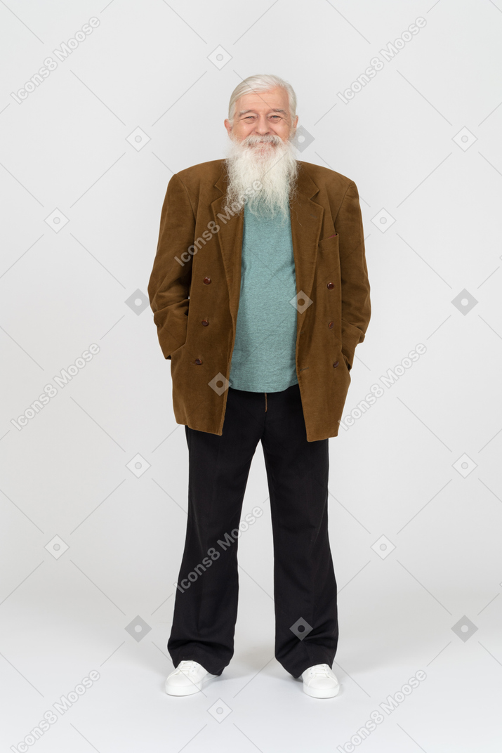 Пожилой мужчина держит руки в карманах и улыбается в камеру