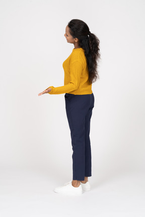 Vista lateral de uma garota com roupas casuais em pé com a mão estendida