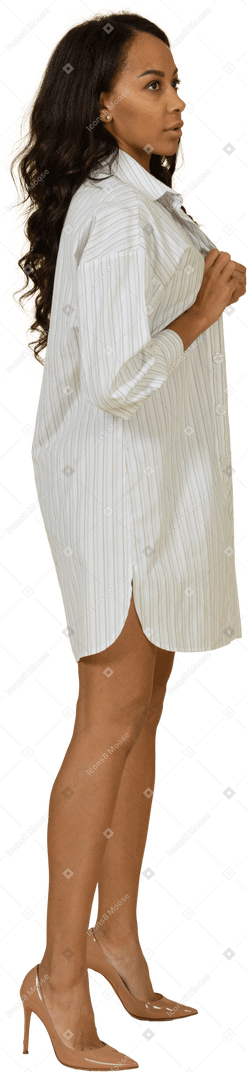 Vue latérale d'une jeune femme à la peau sombre boutonnant sa robe blanche