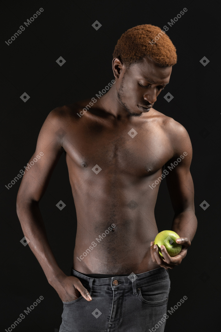 Мускулистый вдумчивый мужчина держит яблоко в темноте