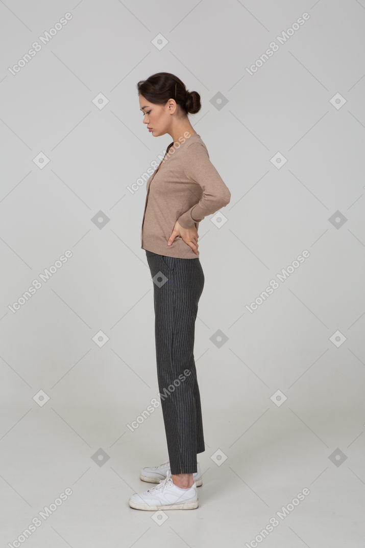 Side view of a young lady in pullover and pants putting hands on hips and looking down