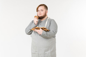 Un gros homme mangeant des biscuits avec un regard insatisfait