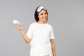 Jovem mulher indiana em roupas confortáveis e com máscara de dormir segurando o iogurte