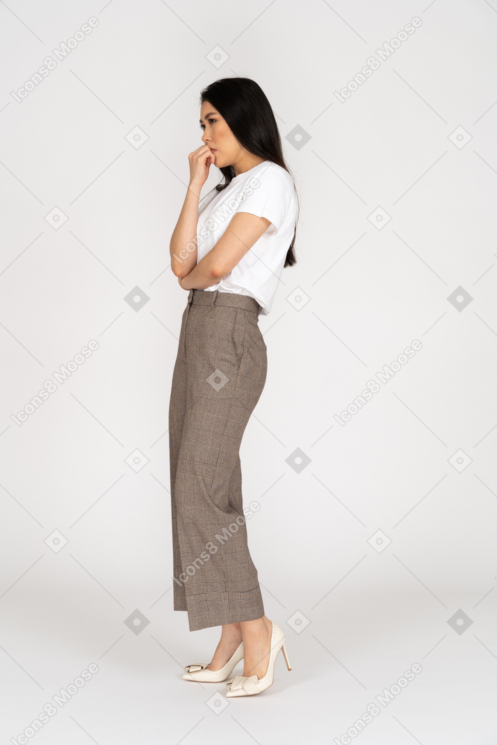 Side view of a suspicious young lady in breeches and t-shirt touching mouth