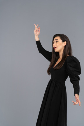Vista lateral de uma jovem em um vestido preto levantando a mão