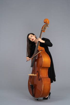 Three-quarter view of a young woman in black dress playing the double-bass with a bow