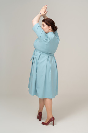 Vista posteriore di una donna in abito blu in posa con le mani sopra la testa