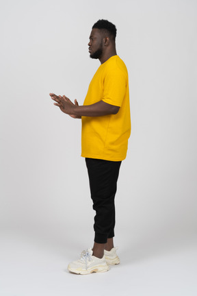 Vista laterale di un giovane uomo dalla pelle scura in maglietta gialla che allunga le braccia