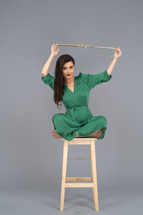 Девушка в полный рост, держащая кларнет над головой, сидя на деревянном стуле