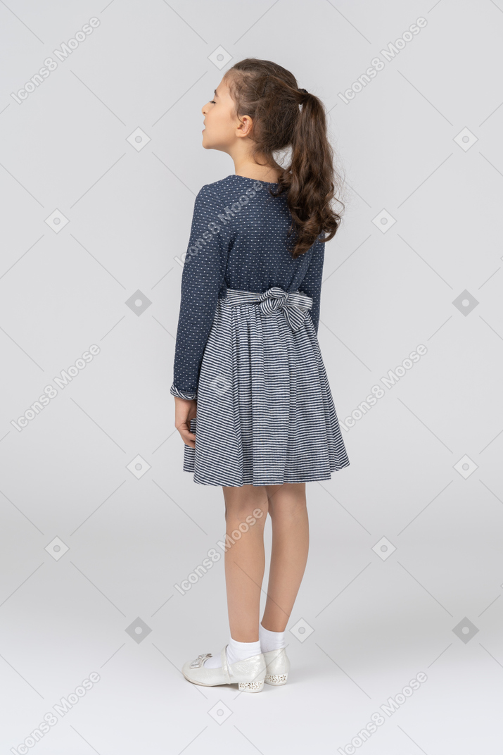 Back view of a girl in casual clothes standing with arms at sides