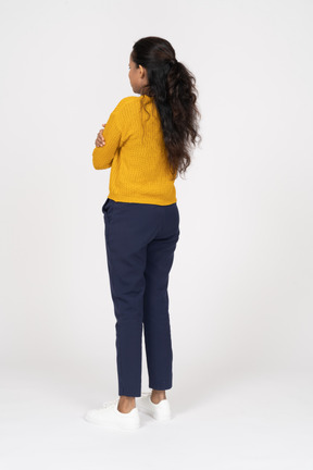 Rear view of a girl in casual clothes standing with crossed arms