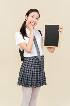 Мечтательная азиатская школьница держит маленькую доску