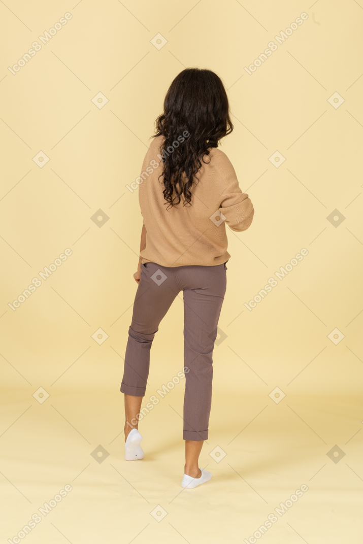Vista posterior de una mujer joven de piel oscura bailando doblando la rodilla