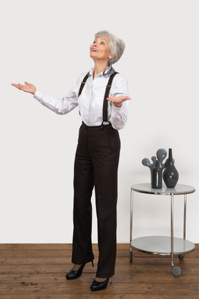 Three-quarter view of an old lady in office clothing raising hands while looking for something