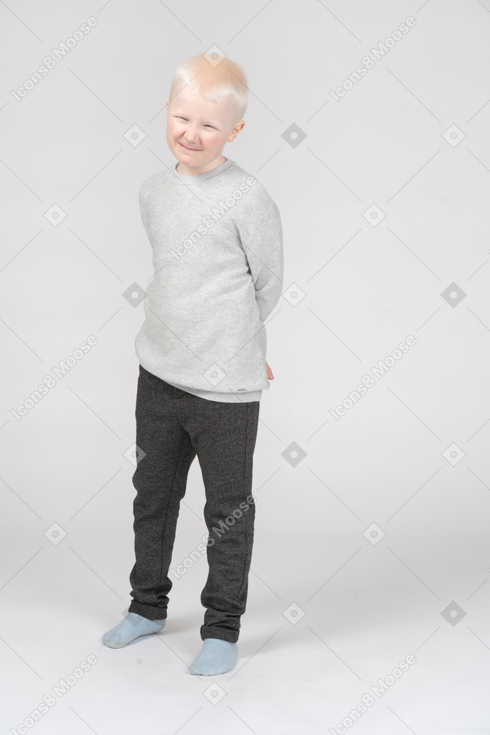 Front view of a grimacing kid boy hiding hands behind