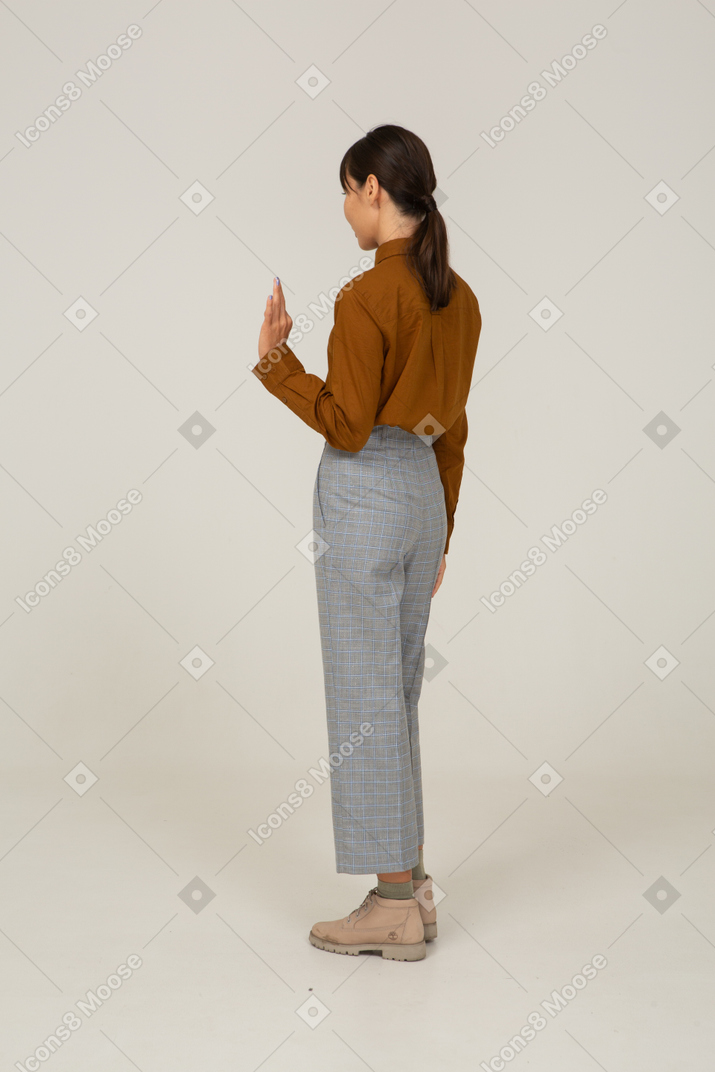 一位身着马裤和衬衫的年轻亚洲女性的四分之三后视图，显示出 ok 的手势