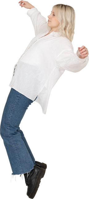 Vista lateral de una mujer rubia de pie de puntillas y extendiendo los brazos